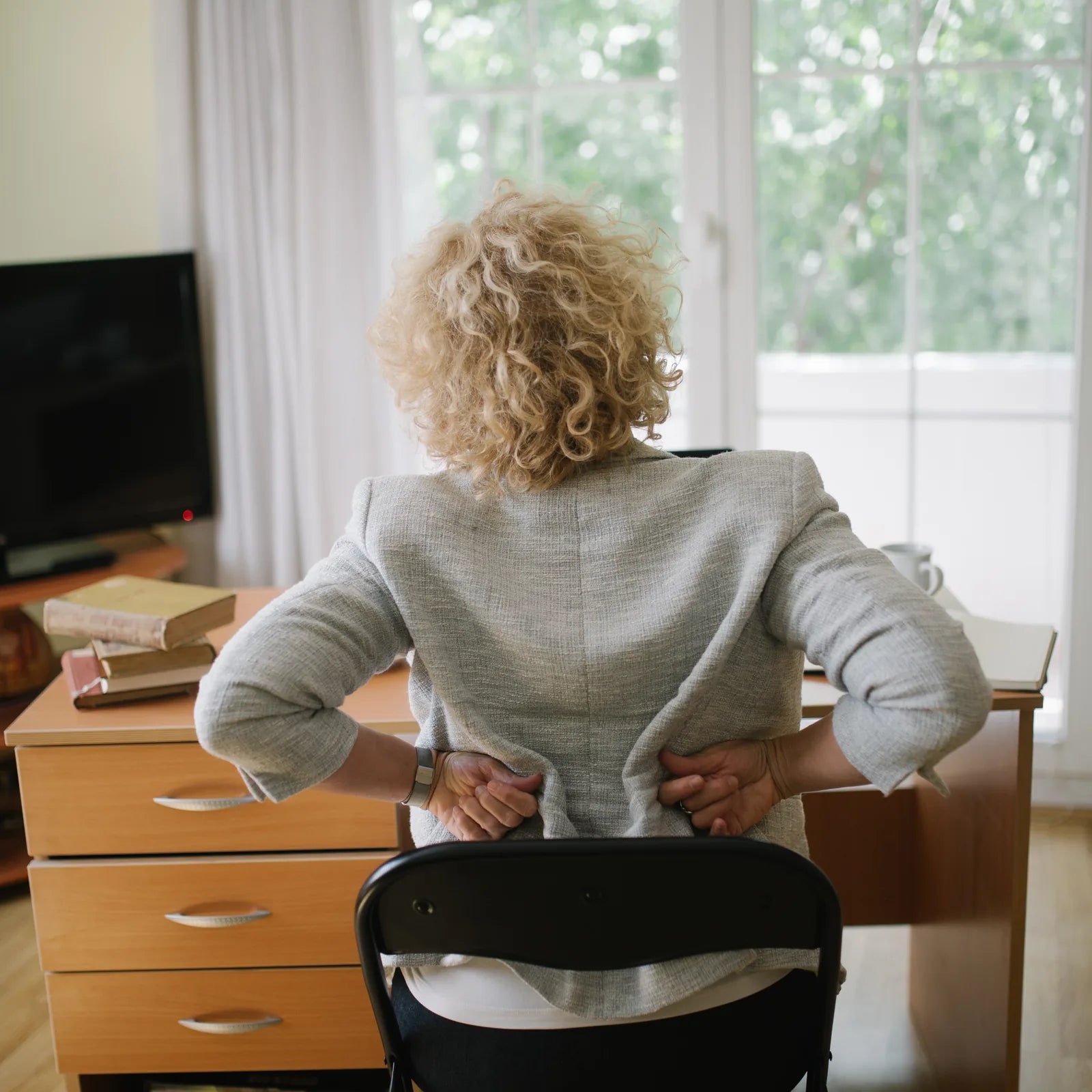 Older woman seated at home with both hands on her lower back