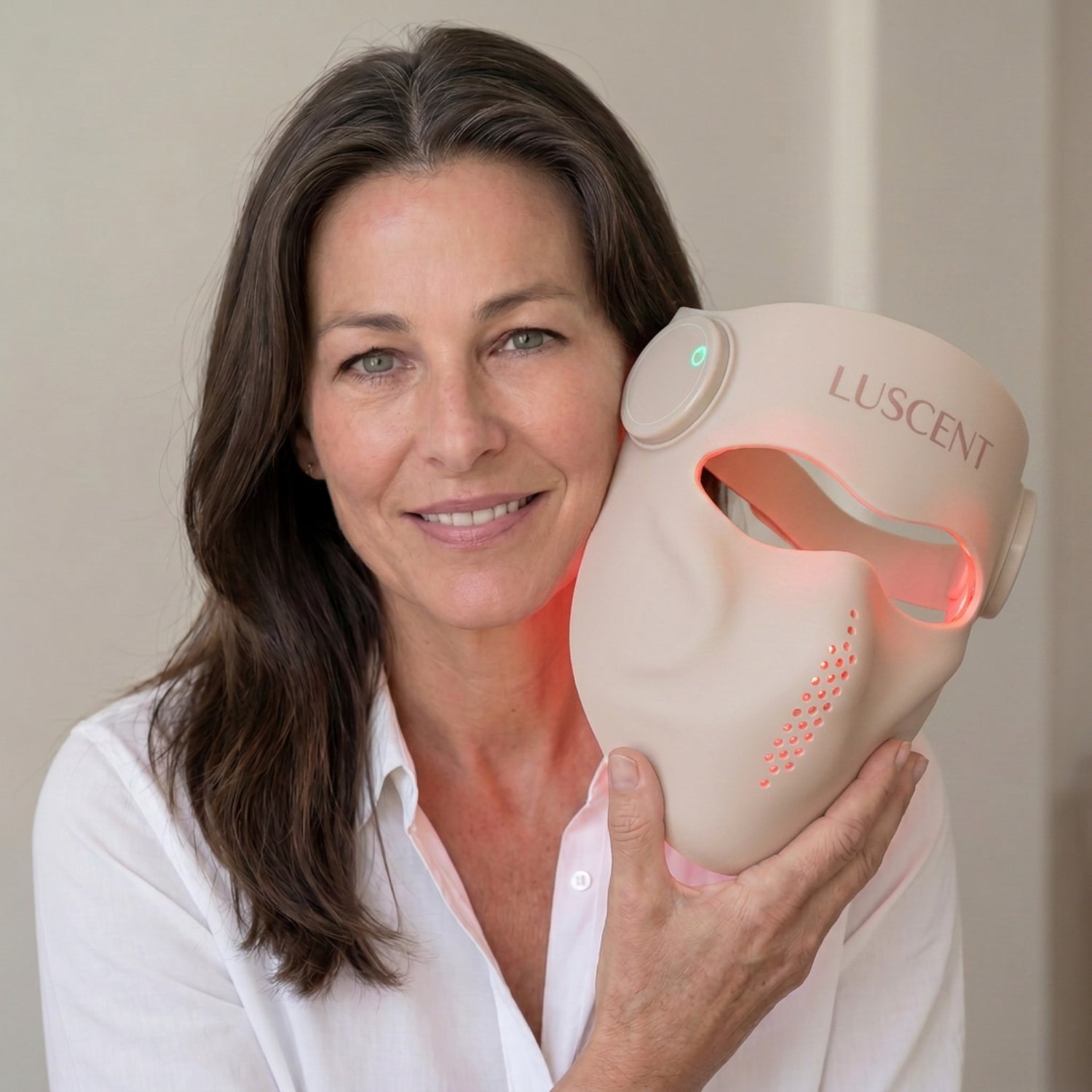 Woman holding a Luscent red light therapy face mask against a neutral background