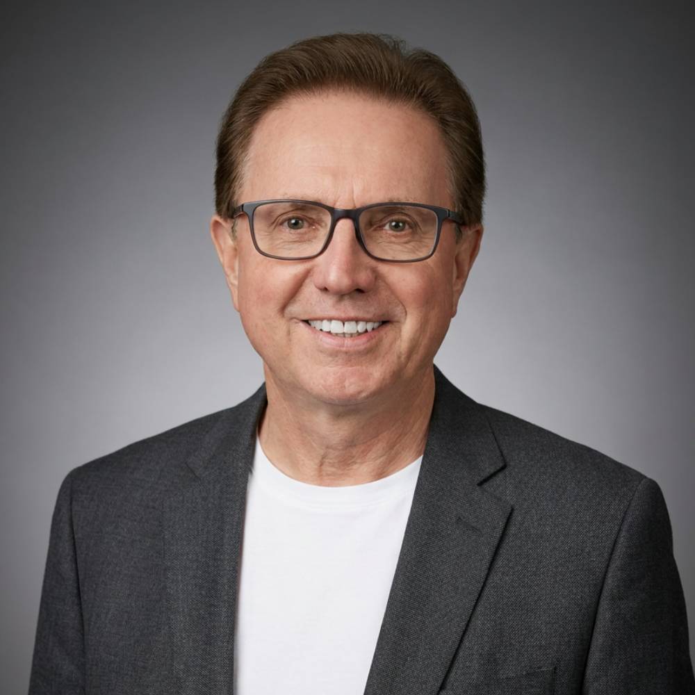 Man wearing glasses and a gray blazer over a white shirt on a gray background