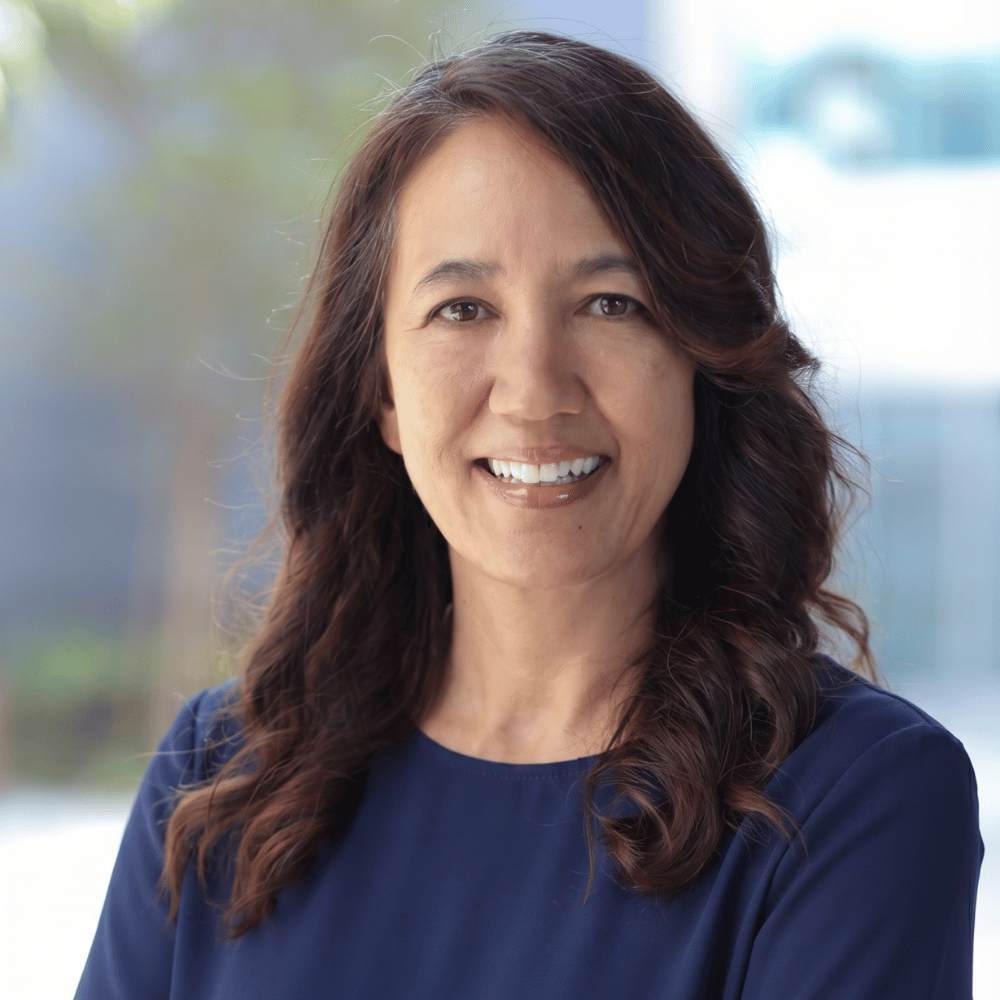 Woman with long brown hair wearing a blue shirt outdoors
