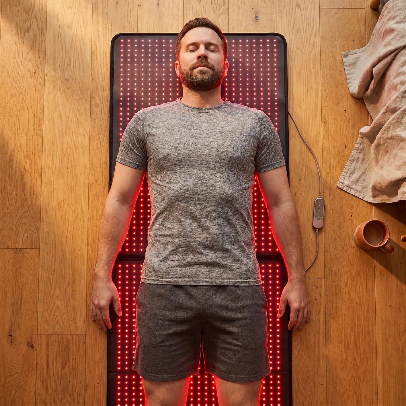 Overhead view of a person lying full length on the glowing red mat on a timber floor
