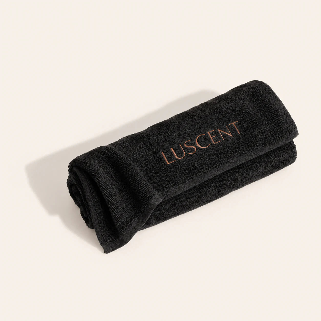 Black Luscent sauna blanket towel insert folded and rolled on an ivory background