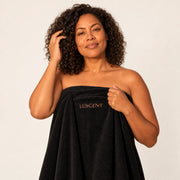 Woman holding a black Luscent sauna blanket insert with one hand near her curls against an ivory studio background